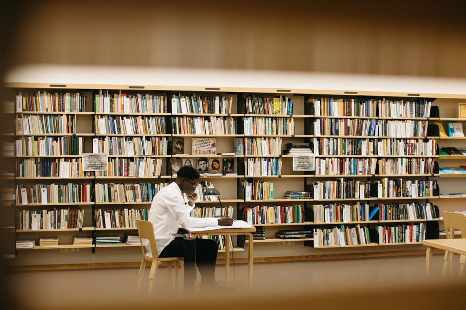 Adult man reading and studying in a well-lit library with bookshelves.