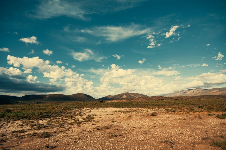 Vast desert terrain with rolling hills under a bright blue sky with scattered clouds.